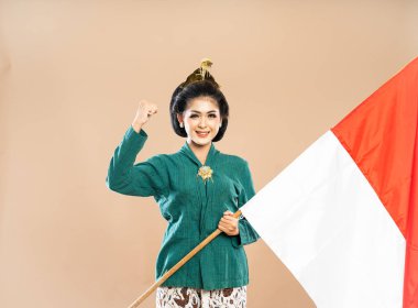 Yeşil kebaya giymiş güzel bir Asyalı kadın kollarını sıkarak Endonezya bayrağını izole edilmiş arka planda tutuyor.