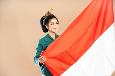 Yeşil kebaya giymiş Asyalı kadın izole edilmiş arka planda Endonezya bayrağını tutuyor.