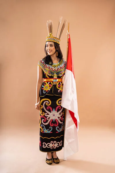 アジア系の女性が白昼の部族の伝統的な服を着てインドネシアの国旗を背景に掲げ — ストック写真