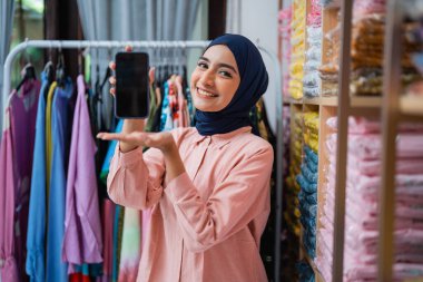 Moda deposunda çalışırken boş ekranını kameraya gösteren tesettürlü bir kadın. çevrimiçi satıcı