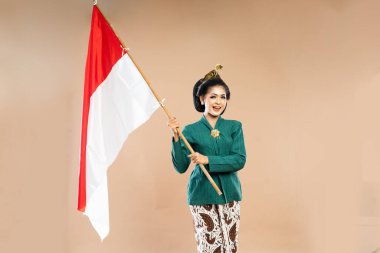 Yeşil kebaya giymiş Asyalı bir kadın gülümseyerek Endonezya bayrağını tutarken iki eli de izole edilmiş arka planda duruyor.