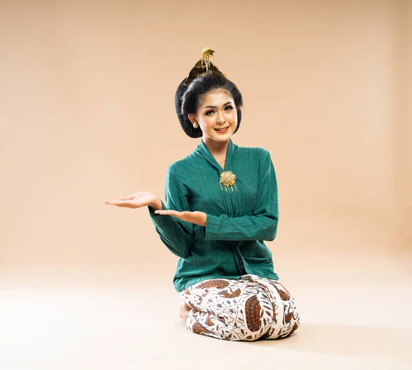 身穿绿色番茄酱的美丽的爪哇女人坐在地板上 一边指指点着孤立的背景 — 图库照片