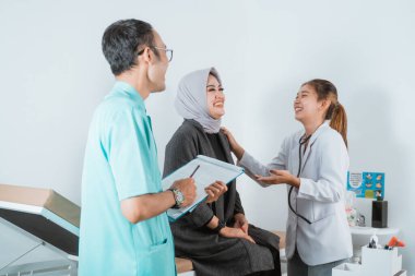 Güzel bir doktor güzel bir hasta ve yatakta oturan kadın hasta için sağlık kontrolü yaparken birlikte gülen yakışıklı bir hemşire.