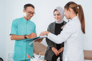 Hemşire üniformalı bir erkek hemşire, kadın doktorla sağlık kontrolü kağıdına yazarken gülümsüyor.