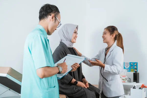 一位女医生笑着摸坐在男护士旁边的女病人的肩膀 她站在男护士旁边 手里拿着医疗检查单 — 图库照片