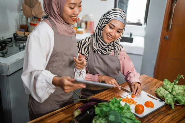 two friend with hijab looking tablet and learn to make new food menu in the kitchen. cooking recipe