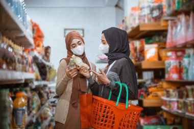 Maskeli iki Müslüman kız bir mağazada alışveriş yaparken eşyaları inceliyor.