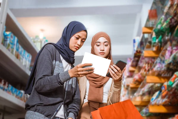 两名穆斯林妇女在超级市场用智能手机检查商品时大吃一惊 — 图库照片