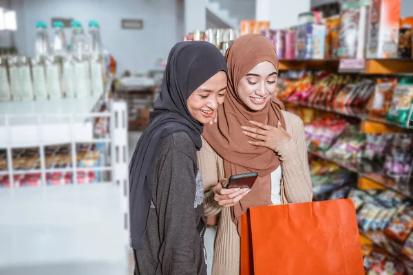 两名亚洲穆斯林女孩在超级市场购物时使用智能手机 — 图库照片