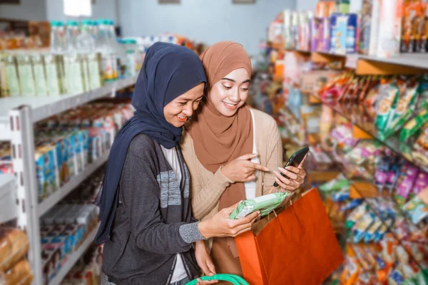 スーパーで買い物をしながらスマホを使っているムスリム女子2人 — ストック写真