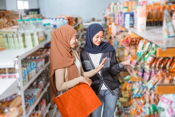 이슬람 소녀는 슈퍼마켓에서 친구들 쇼핑을 하다가 선반에서 물건을 — 스톡 사진