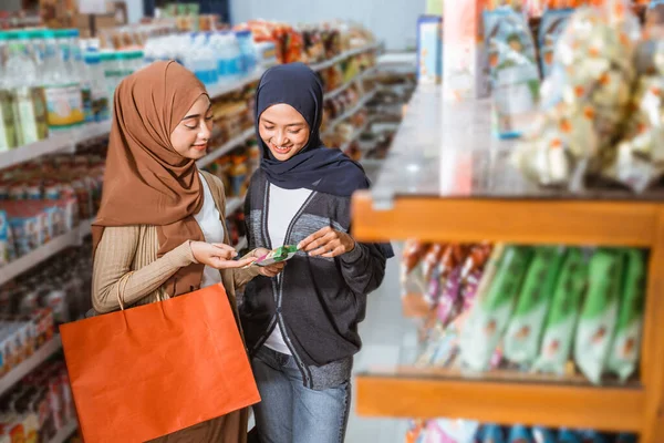 两名穆斯林女孩一边笑着一边拿着超级市场的产品包装 — 图库照片