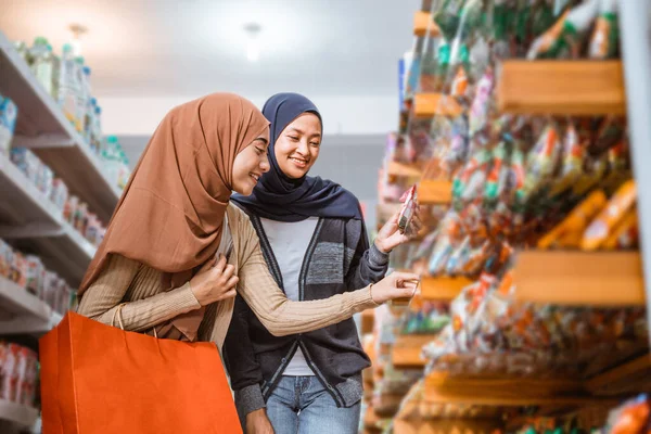 两名穆斯林女孩在超级市场的货架上捡到一件东西 — 图库照片