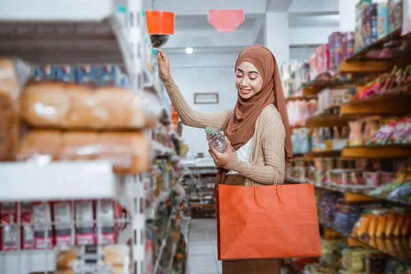在商店购物时 穆斯林女孩一边拿着酒瓶一边挑选商品 — 图库照片