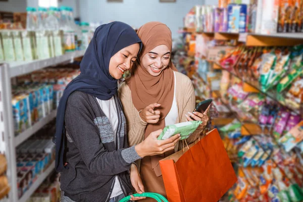 两名穆斯林妇女在超级市场一起购物时使用手机检查物品 — 图库照片