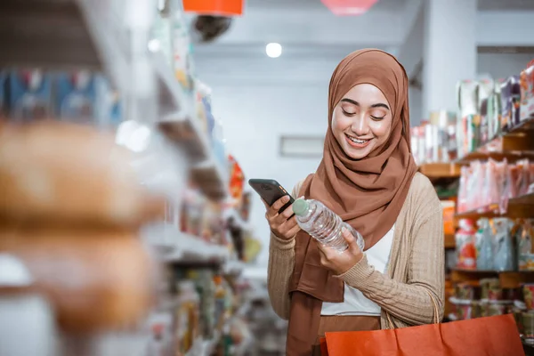 穆斯林女孩在商店购物时拿着手机和酒瓶 — 图库照片