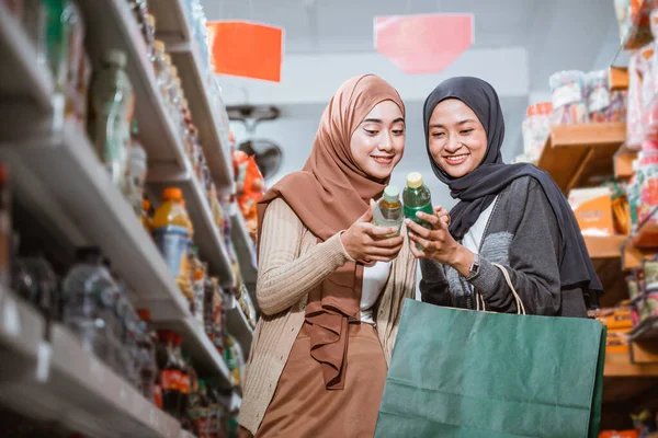 店で一緒に買い物をしながらアイテムを観察マスクの2人のイスラム教徒の女の子 — ストック写真