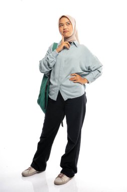 Tesettürlü Asyalı kız öğrenci, izole edilmiş arka planda sırt çantalı fikirler ararken ayakta duruyor.
