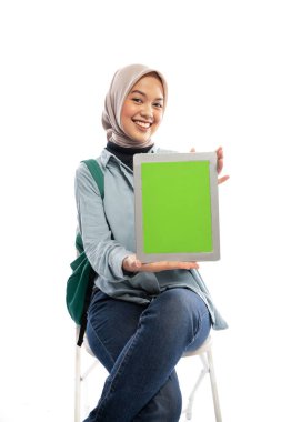tesettürdeki üniversite öğrencisi beyaz arkaplanda otururken boş tablet ekranı gösterir
