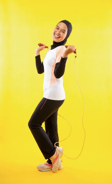 亚洲穆斯林妇女在黄色背景下练习跳绳的侧视图 — 图库照片