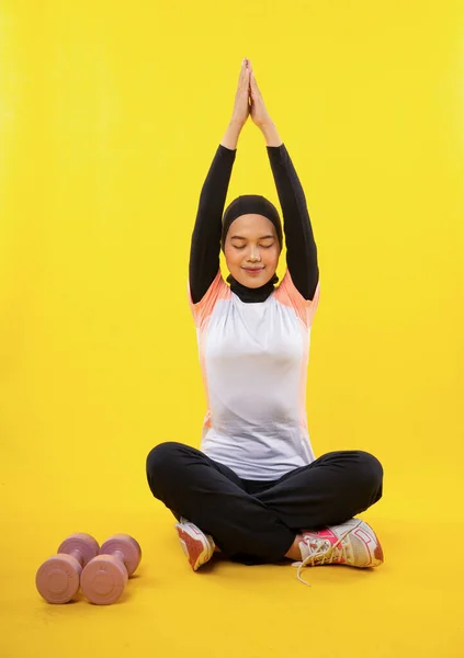 アジアのイスラム教徒女性でスポーツウェアは黄色の背景に一緒に手でヨガを練習座っている — ストック写真