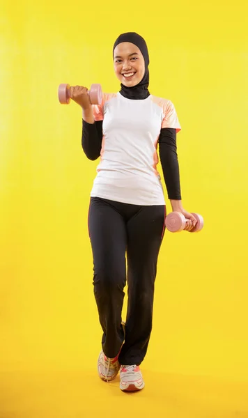 女性のムスリマは黄色の背景にダンベルを使い — ストック写真