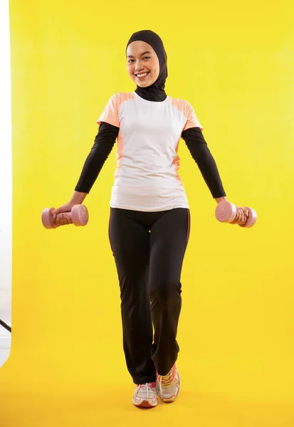 アクティブなイスラム教徒の女性は黄色の背景にダンベルを使用して運動を身に着けている — ストック写真