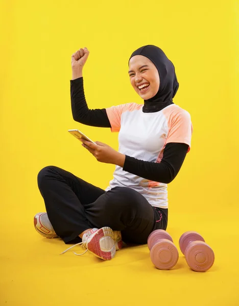 Χαρούμενη Ασιάτισσα Μουσουλμάνα Που Φοράει Αθλητικά Κάθεται Χρησιμοποιώντας Smartphone Κίτρινο — Φωτογραφία Αρχείου