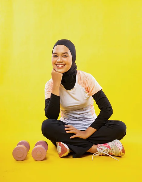 黄色い背景にあごを片手にスポーツウェアを着たアジア系ムスリム女性の笑顔 — ストック写真