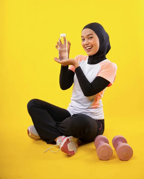 陽気なアジア系ムスリム女性でスポーツウェア座っていますとともに水ボトル上の黄色の背景 — ストック写真