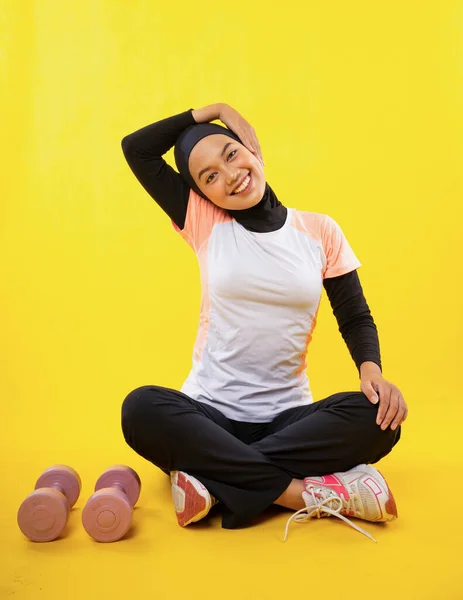 アジアのイスラム教徒女性でHihab身に着けているスポーツウェア座っているストレッチ首の筋肉上の黄色の背景 — ストック写真