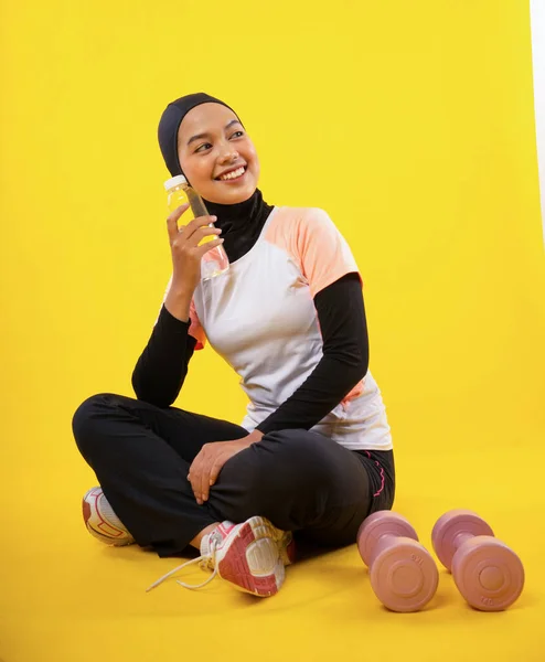身穿运动服的亚洲穆斯林妇女坐在那里 手里拿着一只黄色背景的水瓶 — 图库照片