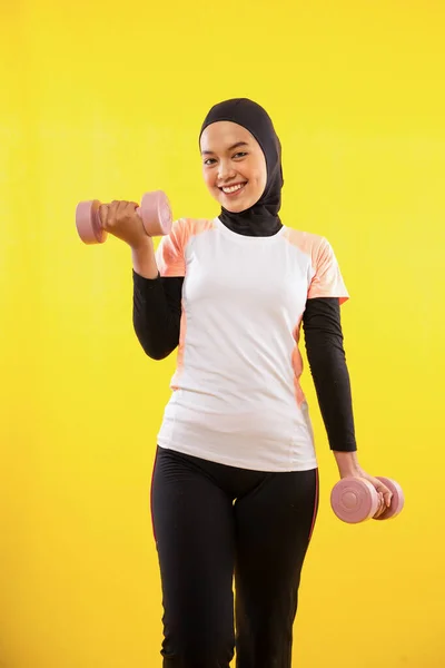 黄色の隔離された背景にダンベルを使用して運動アジアのイスラム教徒の女性 — ストック写真