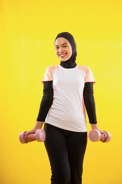 幸せなイスラム教徒の女性運動使用ダンベル上の孤立した黄色の背景 — ストック写真