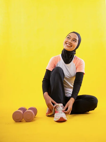 穿着运动服的快乐的穆斯林妇女坐在黄色的背景上固定鞋带 — 图库照片