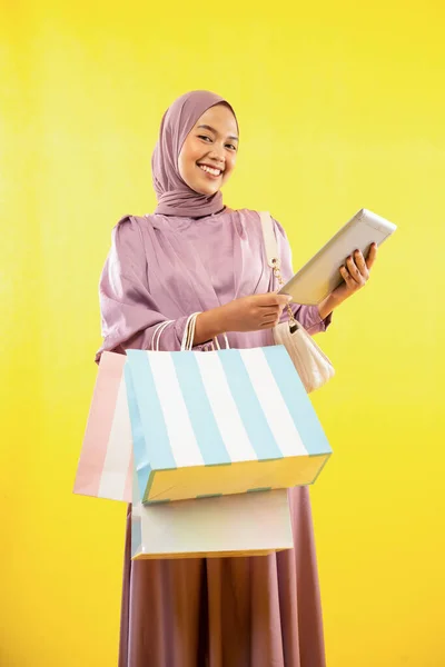 Азиатка Розовом Платье Хиджаба Держит Планшет Сумку Покупок Желтом Фоне — стоковое фото
