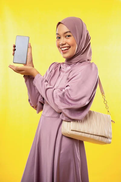 迷人的亚洲穆斯林女人在黄色背景上显示空白的手机屏幕 — 图库照片