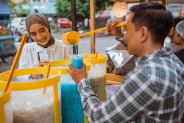 Adam kadın müşterisine renkli içecek ve meyve suyu kavanozunda satıyor. Sokak yemekleri satıcısı.