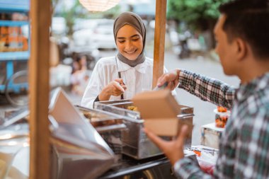 Adam yol kenarında el arabası olan çeşitli hamur köfteleri satıyor.