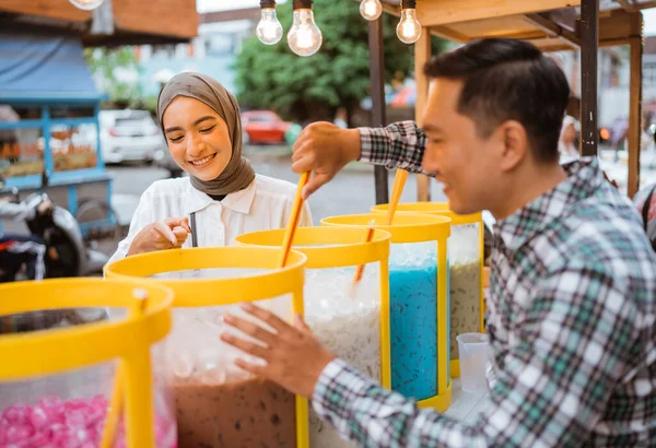 man sells colorful drink and juice in a jar to his female customer. street food vendor