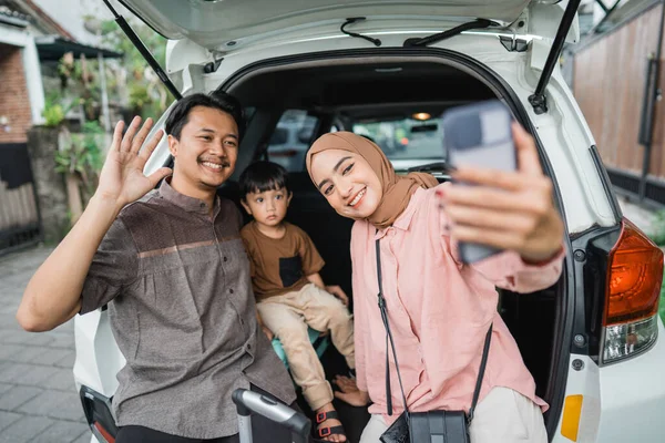 幸せなアジア系イスラム教徒の家族がトランクに座ってスーツケースを持って自撮り写真を撮る — ストック写真