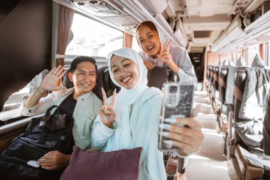 Üç genç insan gülümsüyor ve cep telefonu kameralarına poz veriyor otobüste selfie çekiyorlar.