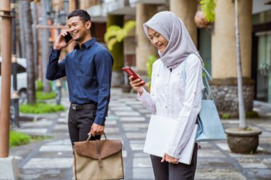 Tesettürlü Asyalı bir kadın cep telefonu kullanıyor. İş adamı yakınından arıyor.