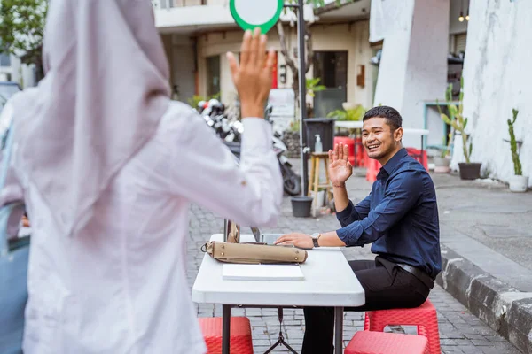 年轻的亚洲男子坐在那里等着 挥手看着蒙面女子来到咖啡店 — 图库照片