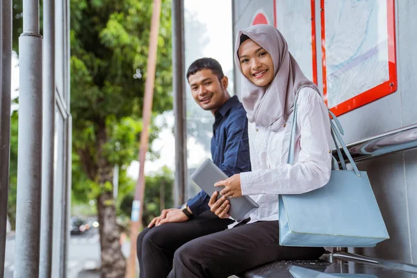 年轻的亚洲男子和蒙面女子坐在巴士站的摄像机前微笑 — 图库照片