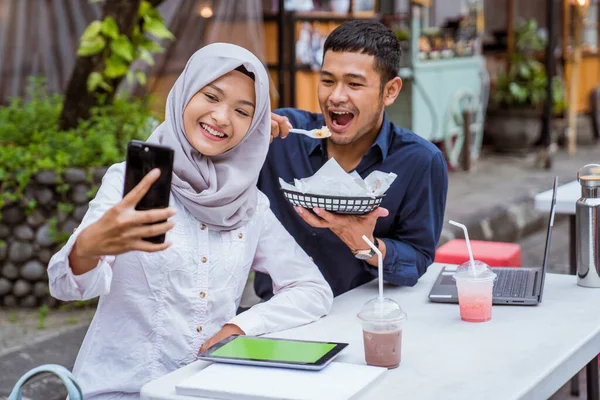 一对年轻的亚洲夫妇一边用手机自拍 一边在咖啡店里大快朵颐 — 图库照片