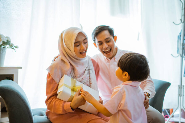 excited mother and father receiving gifts from son during celebration at home. Asian Muslim family concept
