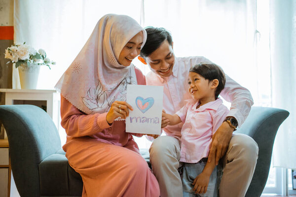 Excited moms and dads receive a paper love drawing from son when together. Asian Muslim family concept