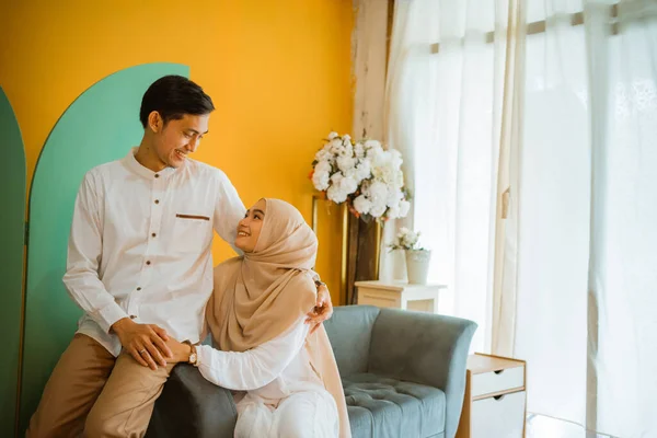 リビングルームで一緒にソファに座っている間 結婚したアジアのイスラム教徒のカップルはお互いを見て — ストック写真