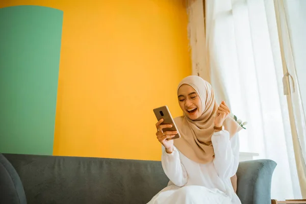 Portrét Vzrušené Asijské Zahalená Žena Sedí Gauči Pomocí Mobilního Telefonu — Stock fotografie